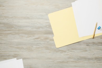 Photo of Paper file folder with blank sheets, pen and binder clip on wooden table, flat lay. Space for text