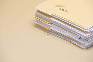 Photo of File folders with documents and paper clips on pale yellow background, closeup. Space for text