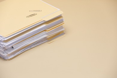Photo of File folders with documents and paper clips on pale yellow background, closeup. Space for text