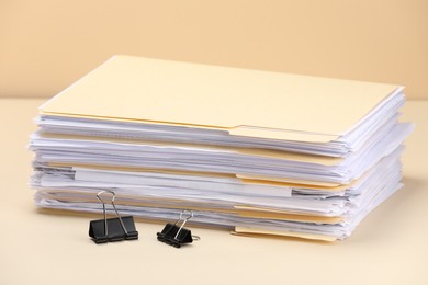 Photo of File folders with papers and binder clips on pale yellow background, closeup