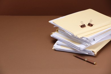 Photo of File folders with papers, pen and binder clips on brown background, space for text
