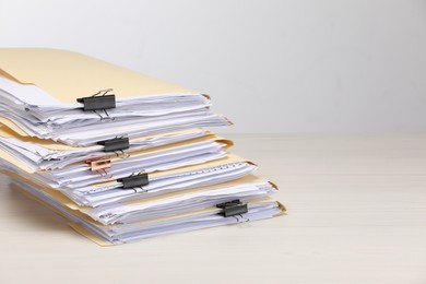 Photo of File folders with papers and binder clips on wooden table against light background, space for text