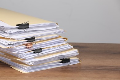 Photo of File folders with papers and binder clips on wooden table against gray background, closeup. Space for text