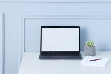 Photo of Laptop, stationery and floral decor on office table near light wall