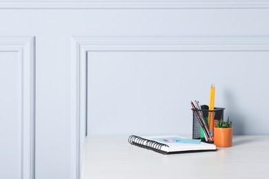 Photo of Different stationery and floral decor on office table near light wall, space for text
