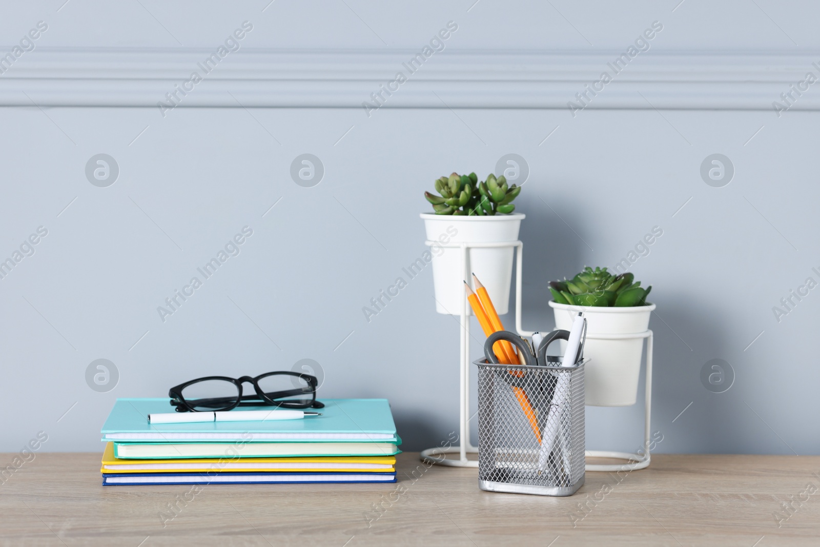 Different stationery, glasses and floral decor on wooden office table near light wall Photo of Different stationery, glasses and floral decor on wooden office table near light wall