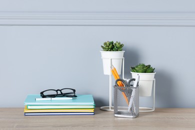 Photo of Different stationery, glasses and floral decor on wooden office table near light wall