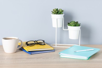 Photo of Different stationery, glasses, coffee and floral decor on wooden office table near light wall