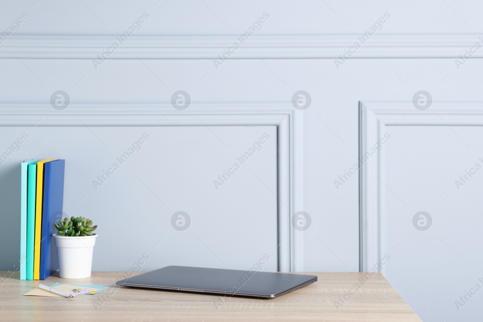 Laptop, stationery and floral decor on wooden office table near light wall Photo of Laptop, stationery and floral decor on wooden office table near light wall