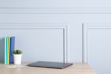Photo of Laptop, stationery and floral decor on wooden office table near light wall