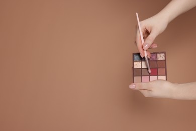 Photo of Woman with eyeshadow palette and brush on beige background, closeup. Space for text