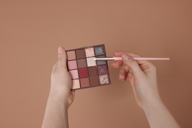 Photo of Woman with eyeshadow palette and brush on beige background, closeup