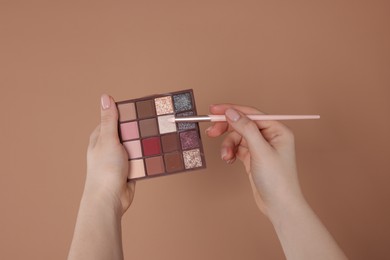 Photo of Woman with eyeshadow palette and brush on beige background, closeup