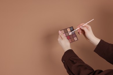 Photo of Woman with eyeshadow palette and brush on beige background, closeup. Space for text