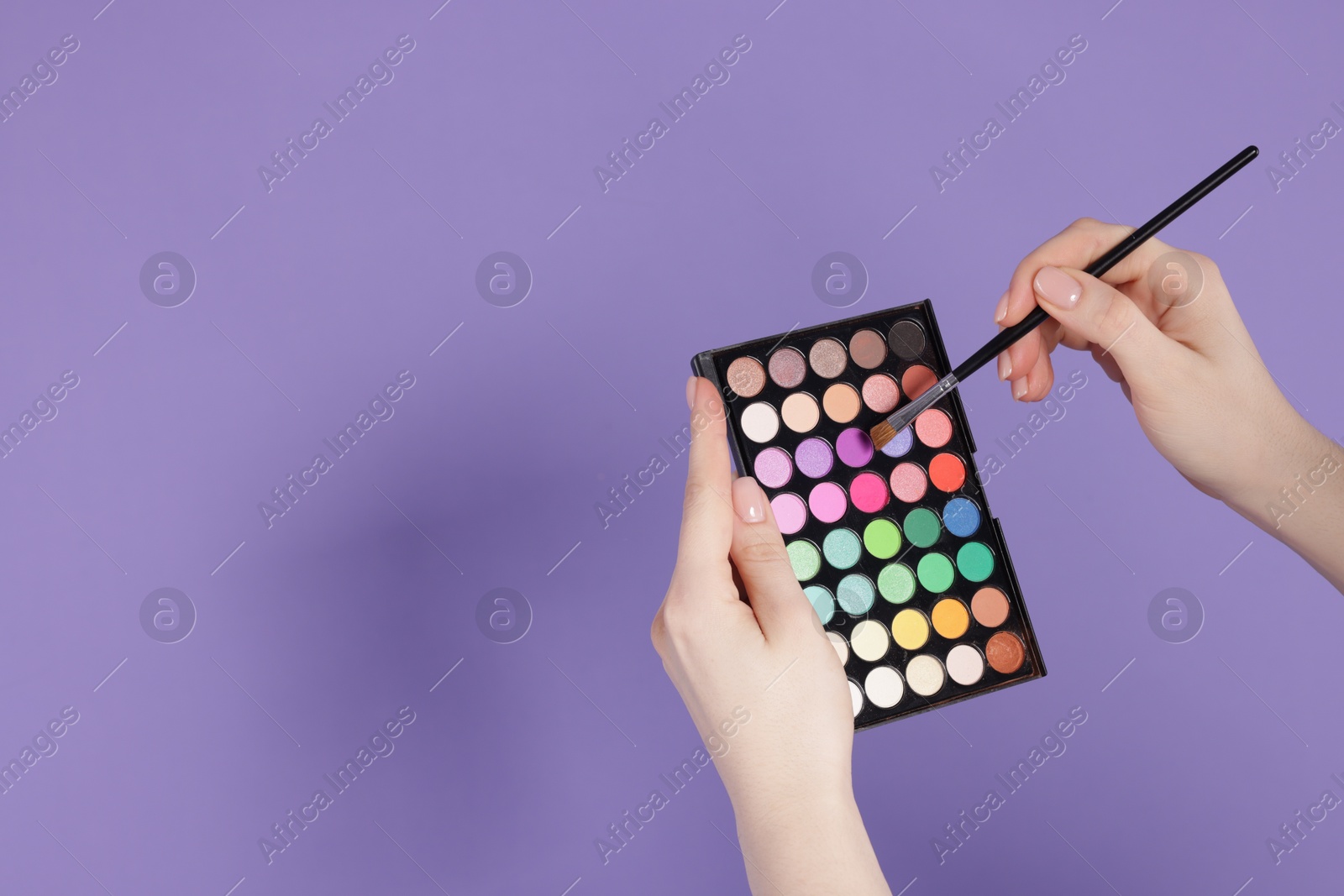 Woman with eyeshadow palette and brush on violet background, closeup. Space for text Photo of Woman with eyeshadow palette and brush on violet background, closeup. Space for text