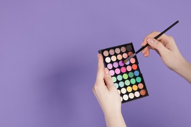 Photo of Woman with eyeshadow palette and brush on violet background, closeup. Space for text