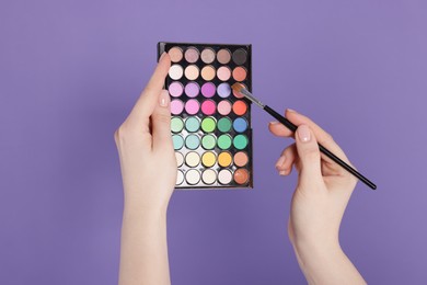 Photo of Woman with eyeshadow palette and brush on violet background, closeup