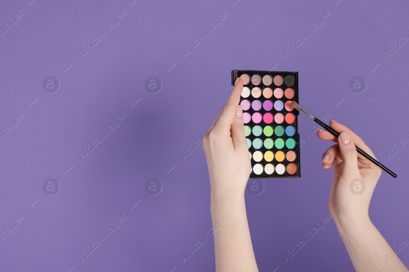 Woman with eyeshadow palette and brush on violet background, closeup. Space for text Photo of Woman with eyeshadow palette and brush on violet background, closeup. Space for text