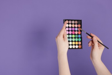 Photo of Woman with eyeshadow palette and brush on violet background, closeup. Space for text