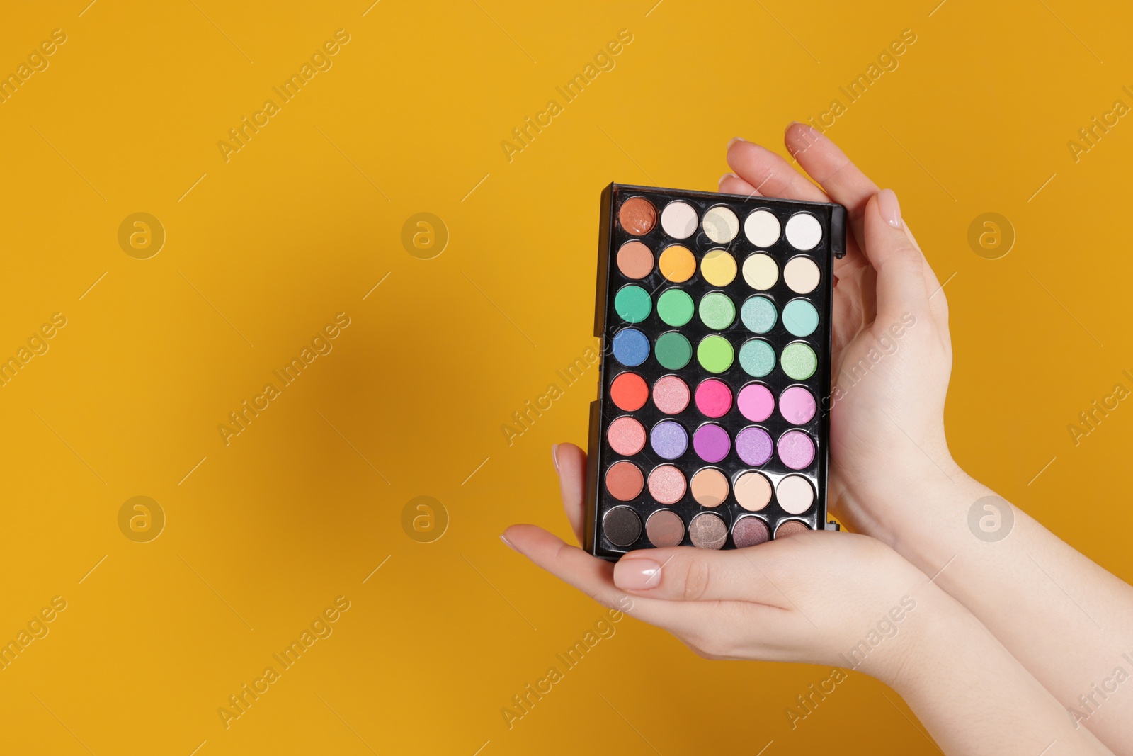 Woman with bright eyeshadow palette on yellow background, closeup. Space for text Photo of Woman with bright eyeshadow palette on yellow background, closeup. Space for text