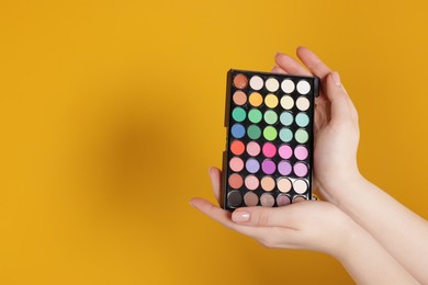Photo of Woman with bright eyeshadow palette on yellow background, closeup. Space for text