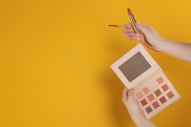 Photo of Woman with eyeshadow palette, lipstick and brush on yellow background, closeup. Space for text
