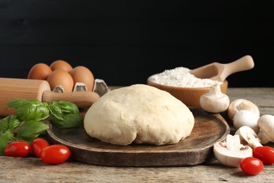 Photo of Making pizza. Different ingredients on wooden table against black background, closeup
