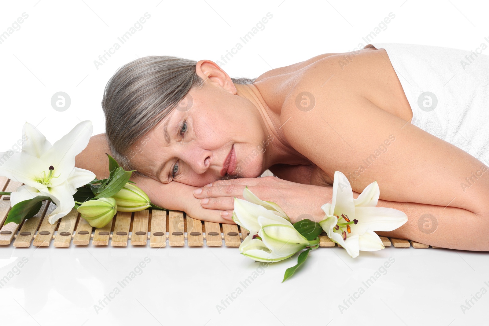 Senior woman with lily flowers relaxing on bamboo mat against white background Photo of Senior woman with lily flowers relaxing on bamboo mat against white background