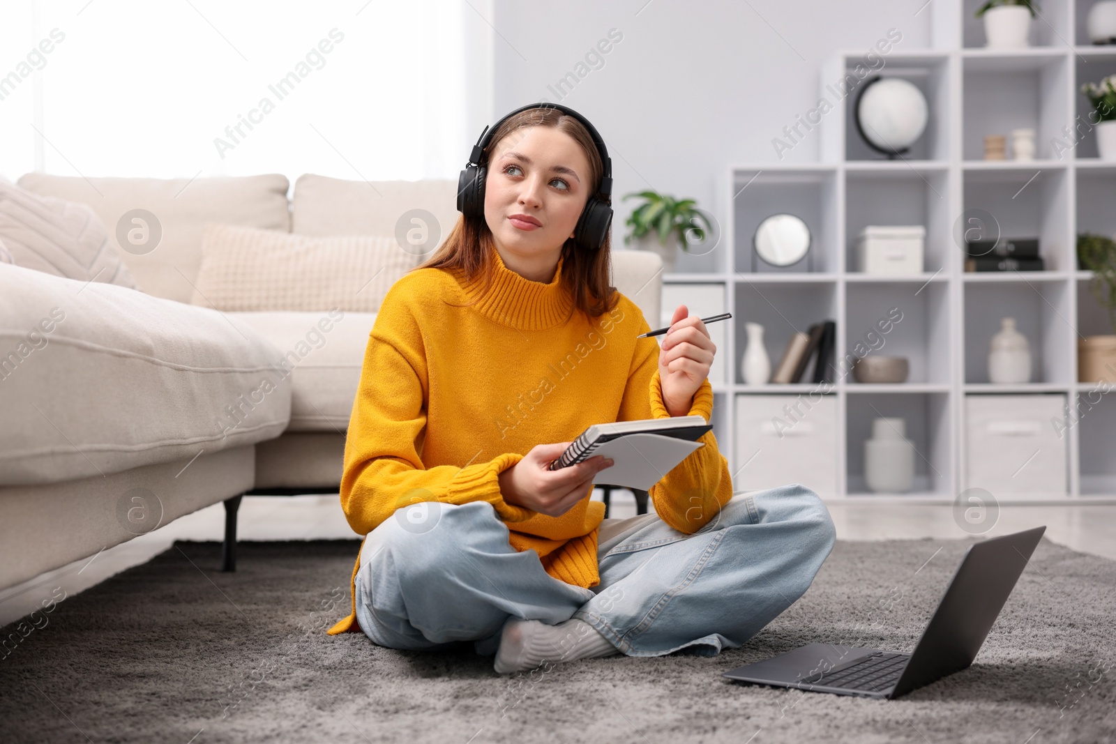 Teenage girl in headphones doing homework near laptop on floor at home Photo of Teenage girl in headphones doing homework near laptop on floor at home