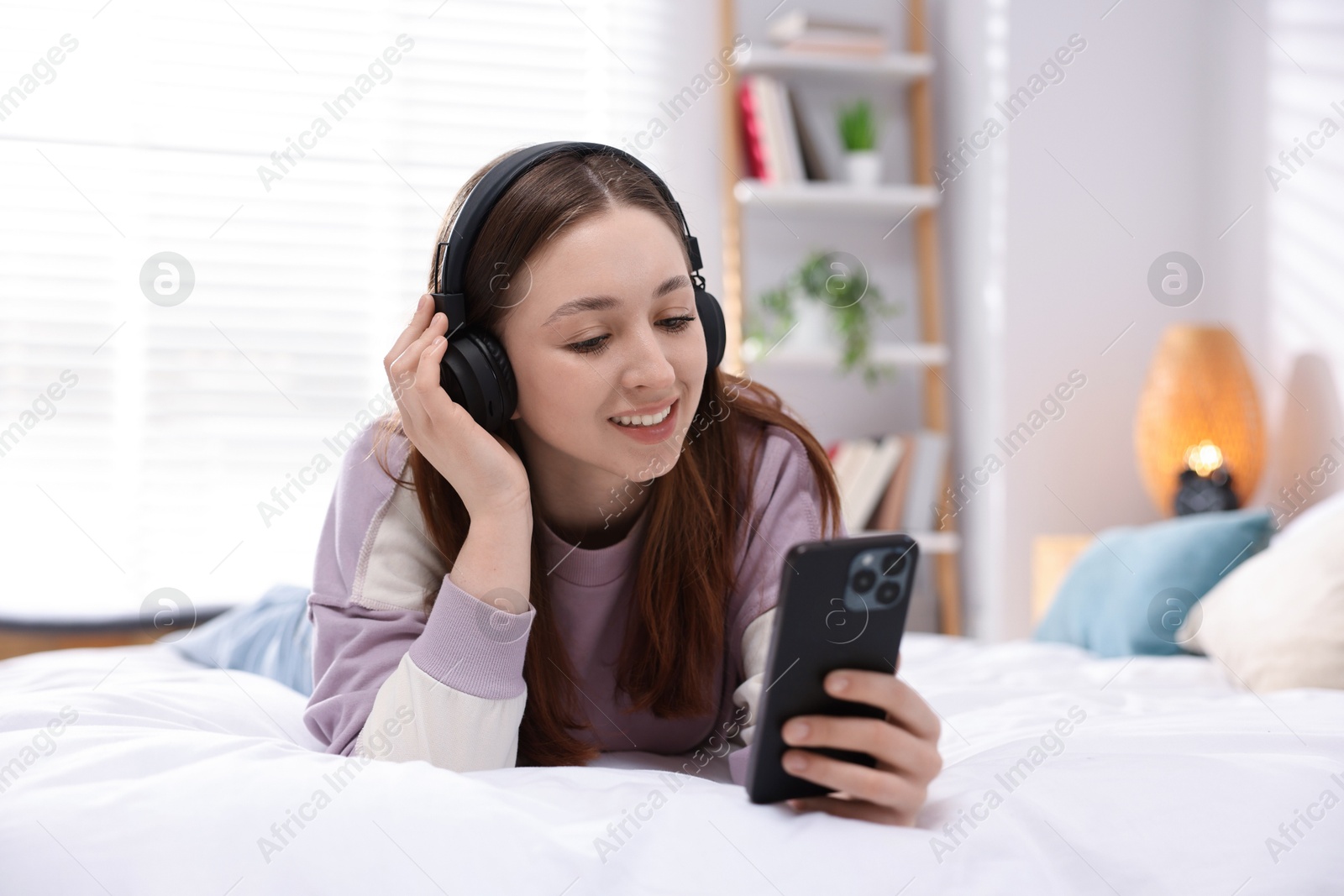 Photo of Teenage girl in headphones using smartphone on bed at home