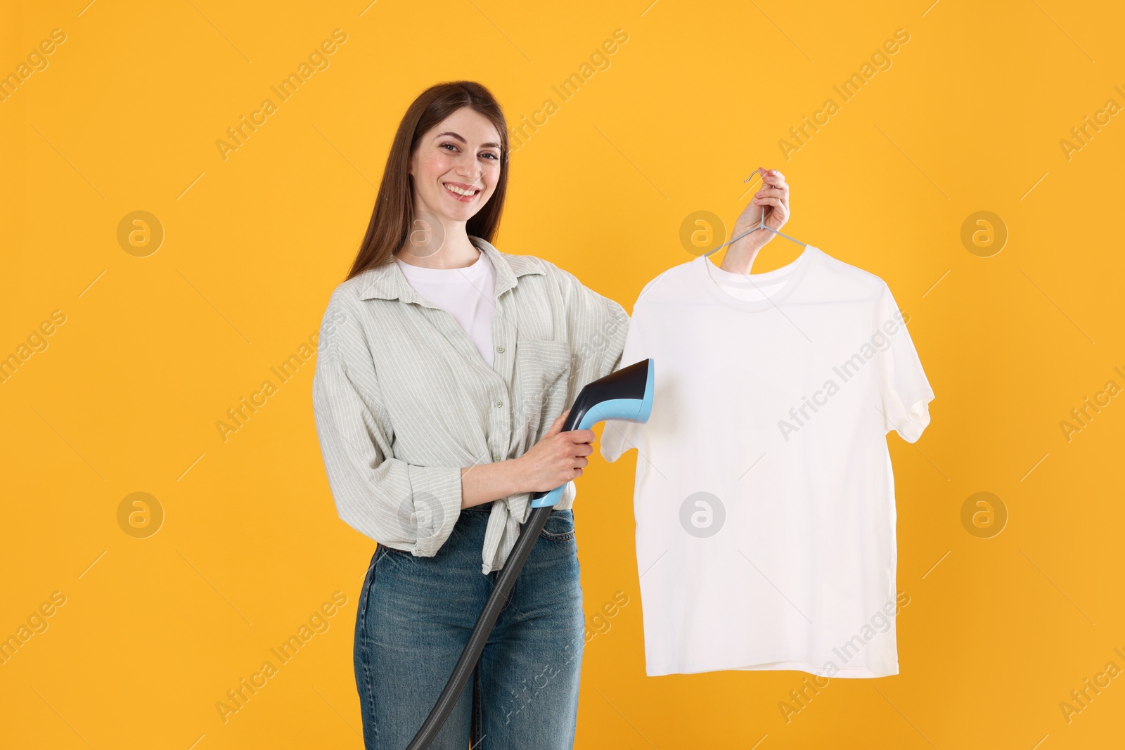 Smiling woman steaming t-shirt on yellow background Photo of Smiling woman steaming t-shirt on yellow background