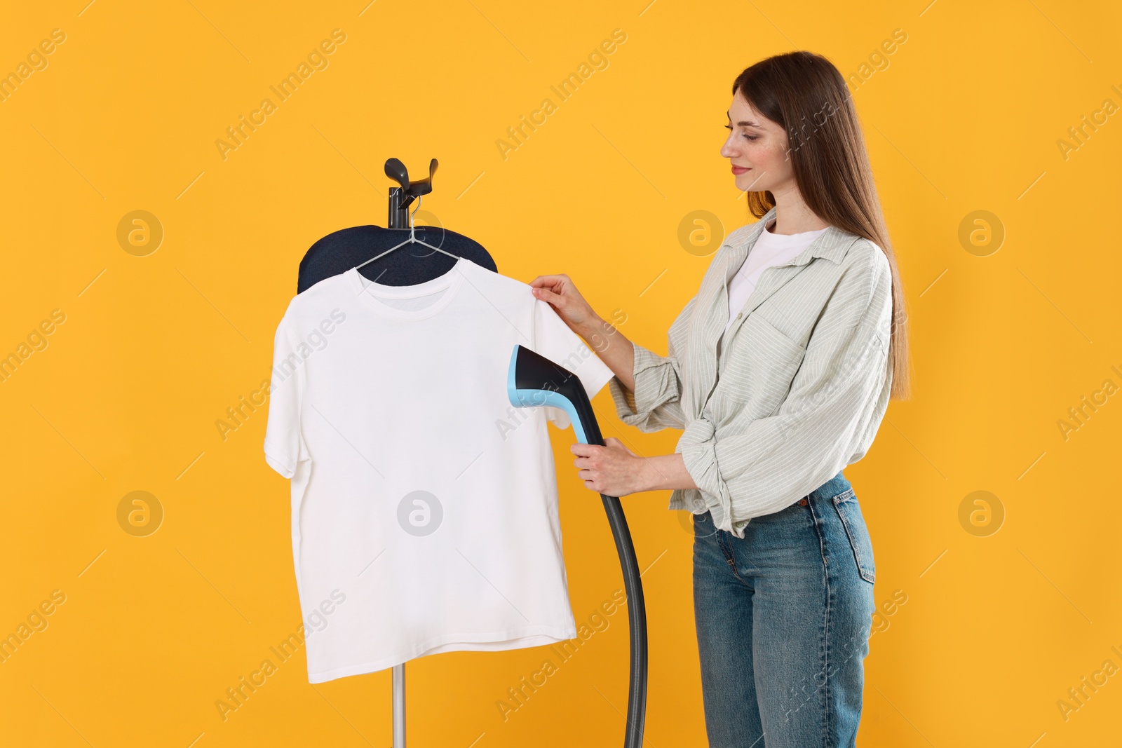 Woman steaming white t-shirt on yellow background Photo of Woman steaming white t-shirt on yellow background