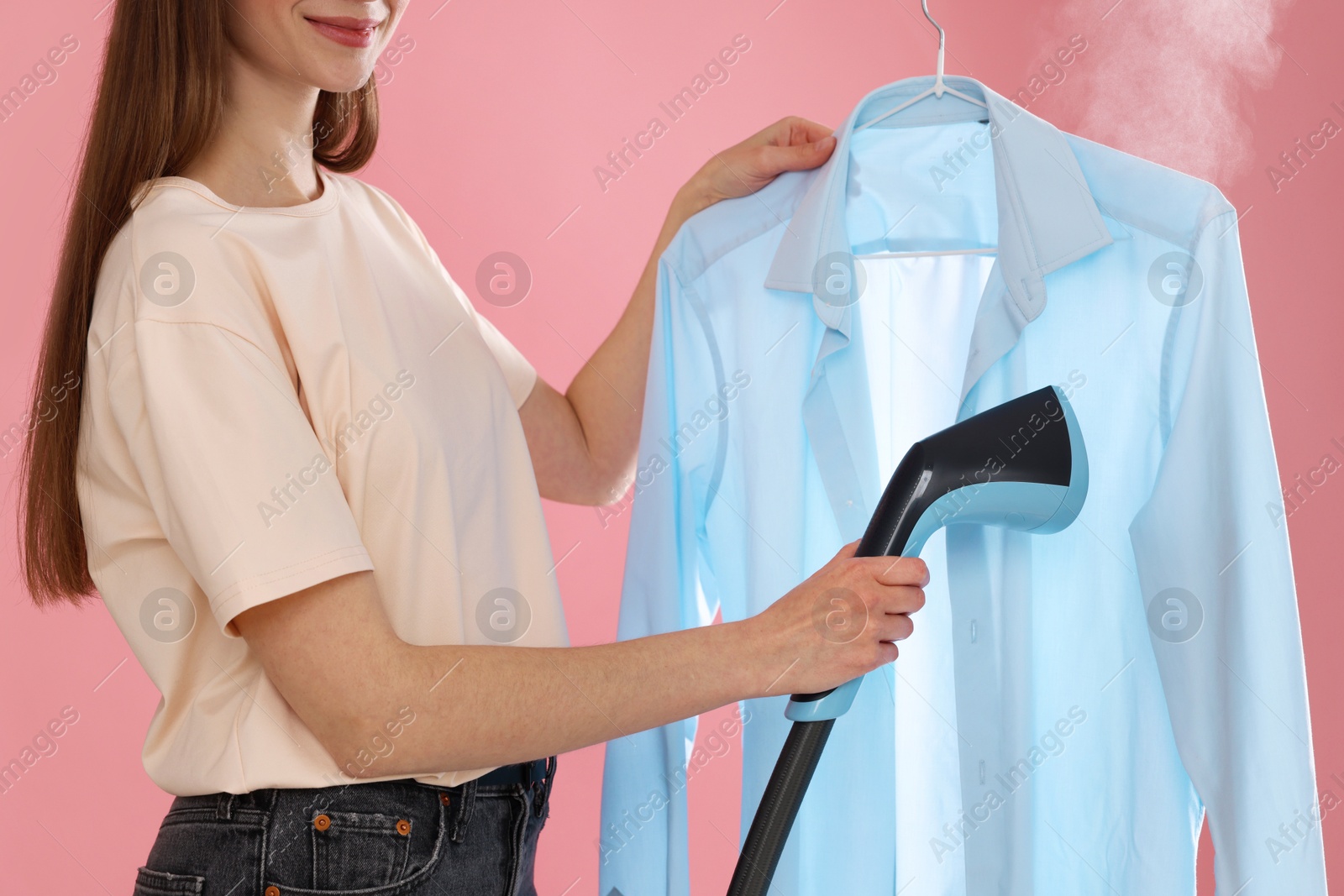 Woman steaming shirt on pink background, closeup Photo of Woman steaming shirt on pink background, closeup