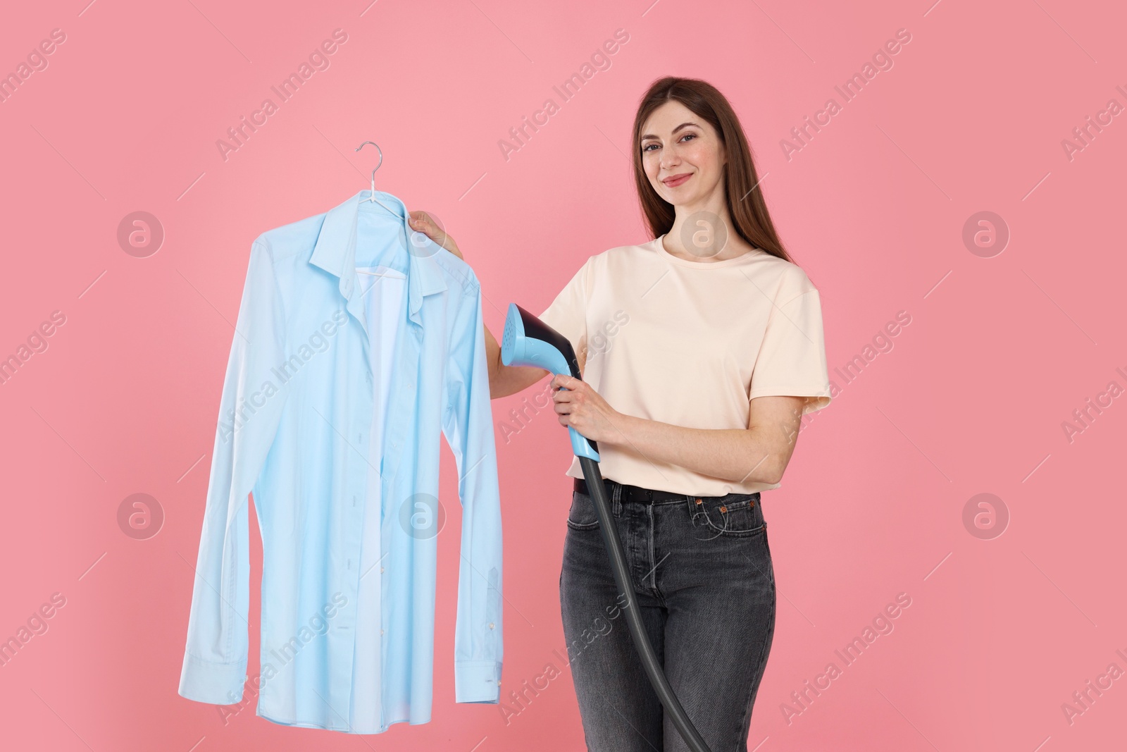 Photo of Beautiful woman steaming shirt on pink background