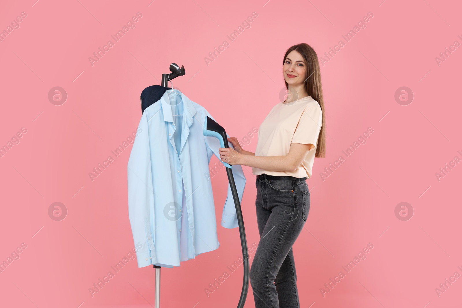 Beautiful woman steaming shirt on stand against pink background Photo of Beautiful woman steaming shirt on stand against pink background