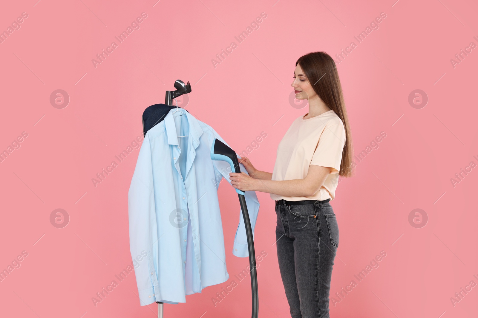 Photo of Beautiful woman steaming shirt on stand against pink background