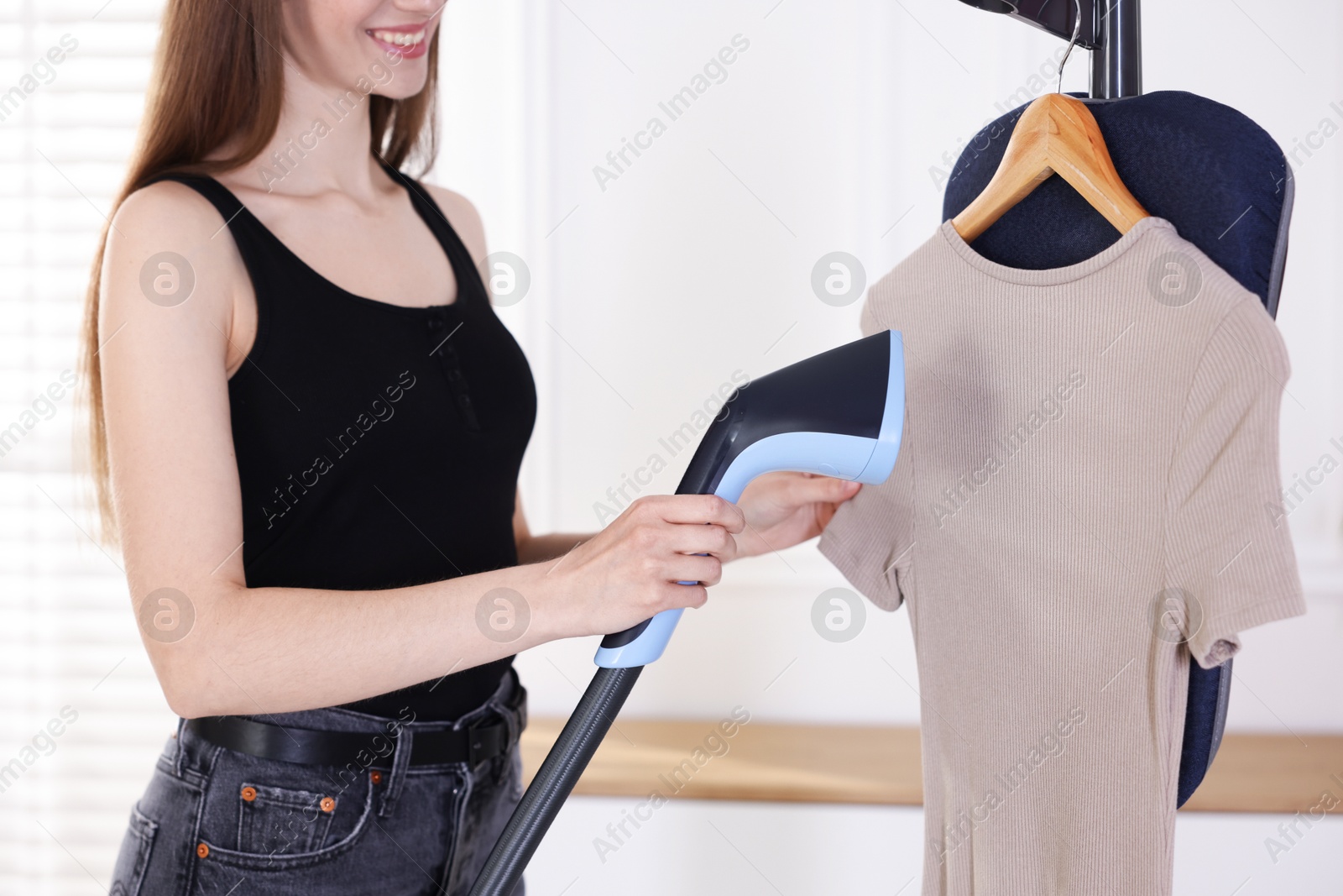 Photo of Smiling woman steaming dress on stand at home, closeup