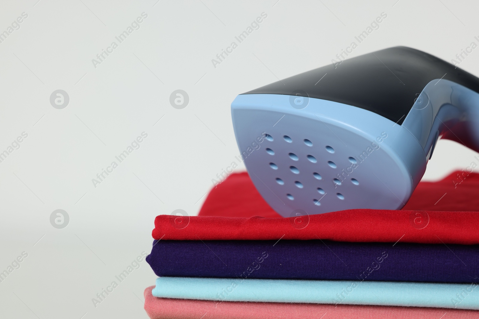 Upright steamer and stack of folded clothes on white table, closeup. Space for text Photo of Upright steamer and stack of folded clothes on white table, closeup. Space for text