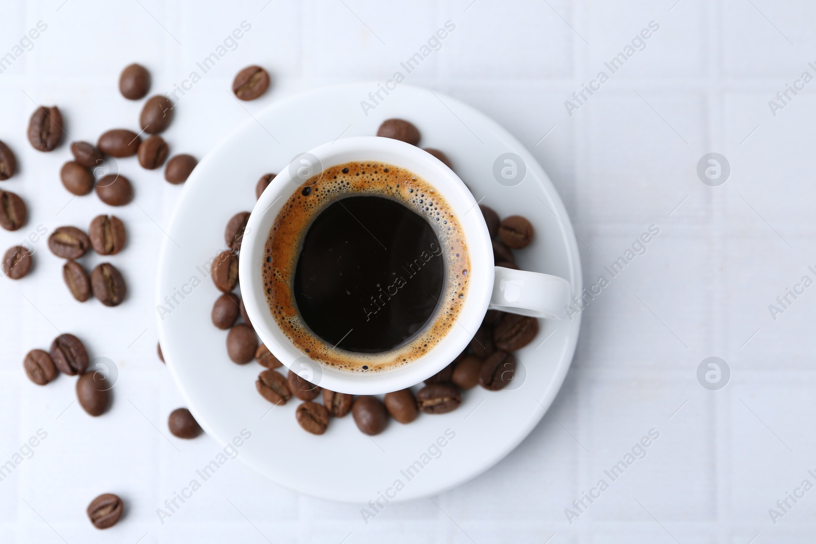 Aromatic coffee in cup and beans on white tiled table, flat lay. Space for text Photo of Aromatic coffee in cup and beans on white tiled table, flat lay. Space for text