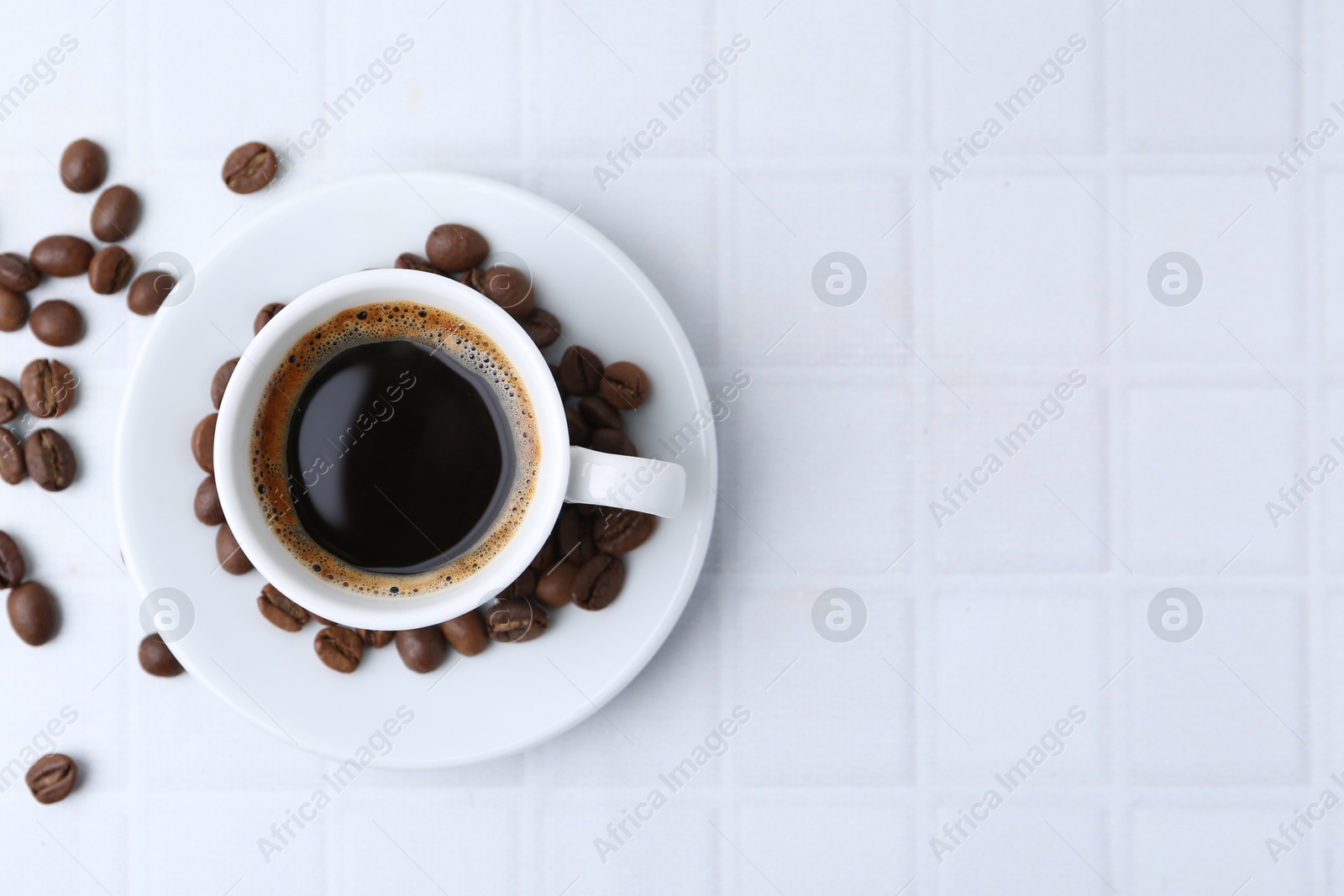 Aromatic coffee in cup and beans on white tiled table, flat lay. Space for text Photo of Aromatic coffee in cup and beans on white tiled table, flat lay. Space for text