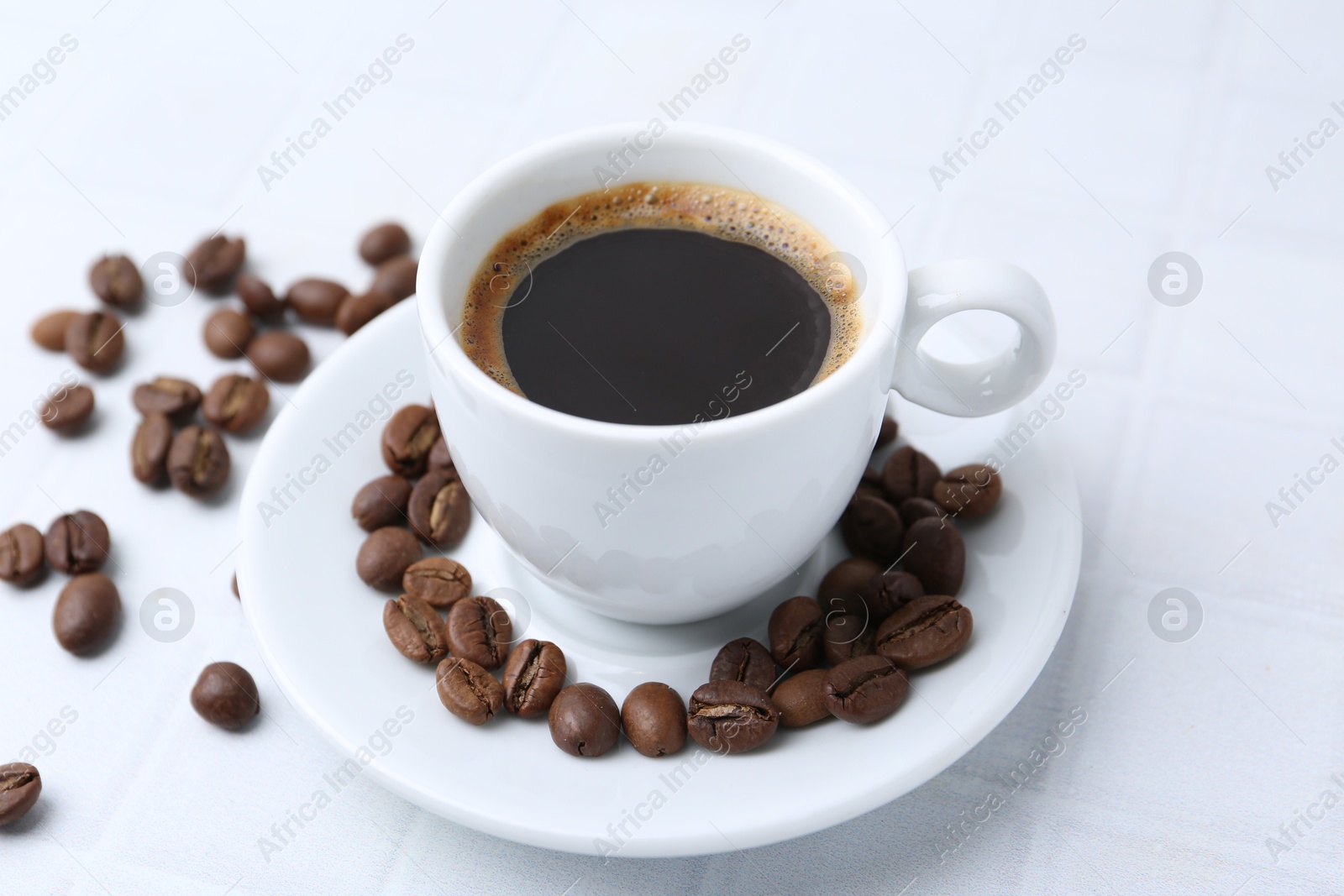 Aromatic coffee in cup and beans on white table, closeup Photo of Aromatic coffee in cup and beans on white table, closeup
