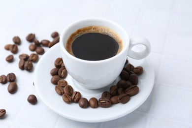 Photo of Aromatic coffee in cup and beans on white table, closeup