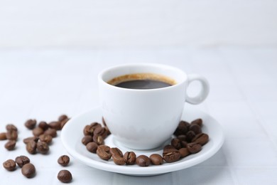 Photo of Aromatic coffee in cup and beans on white table, closeup