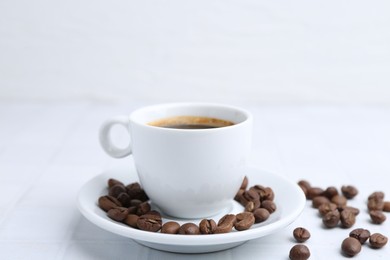 Photo of Aromatic coffee in cup and beans on white table, closeup