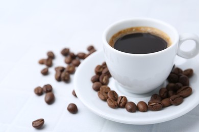 Photo of Aromatic coffee in cup and beans on white table, closeup. Space for text