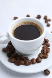 Photo of Aromatic coffee in cup and beans on white table, closeup