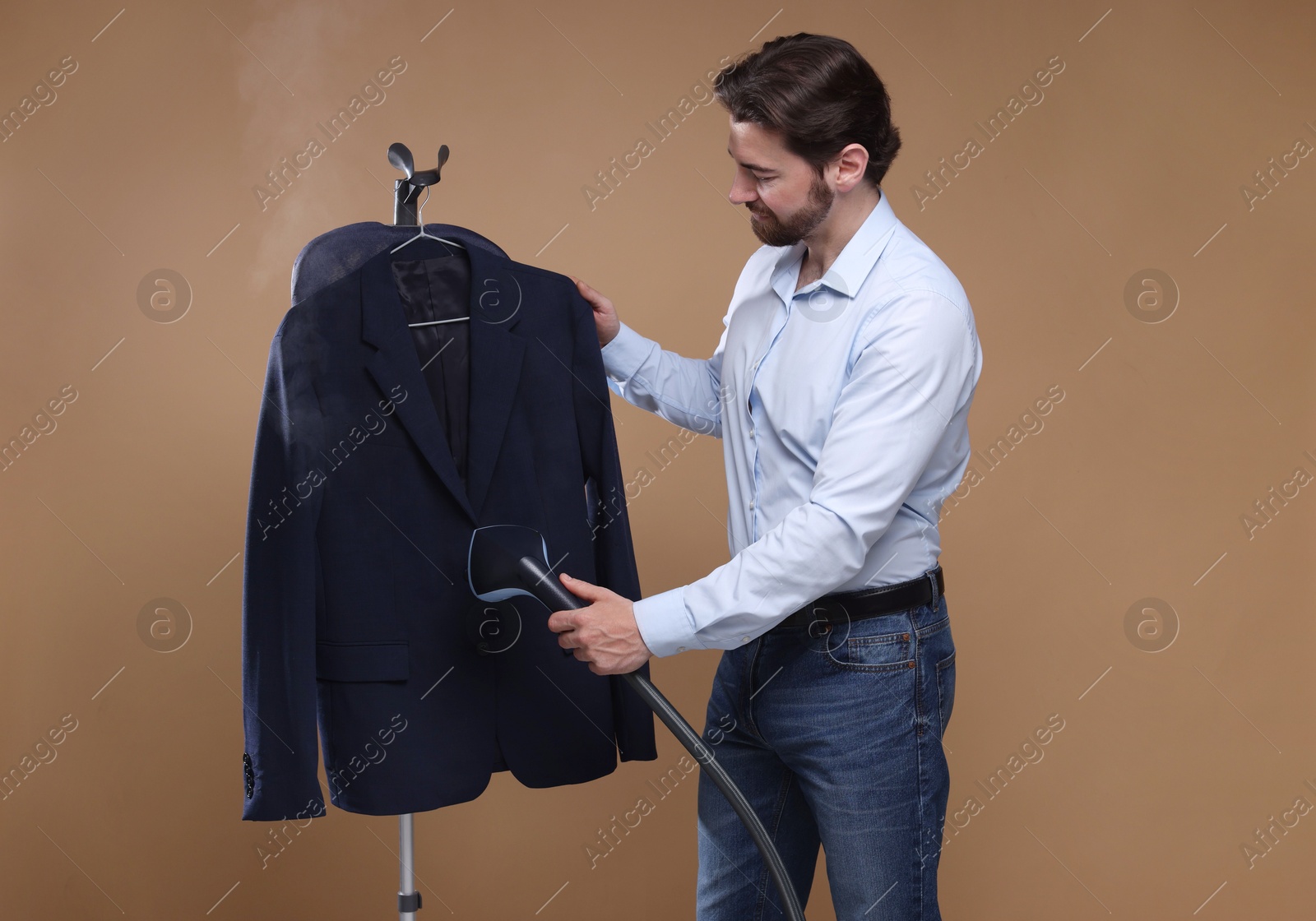 Man steaming jacket with stand steamer on brown background Photo of Man steaming jacket with stand steamer on brown background