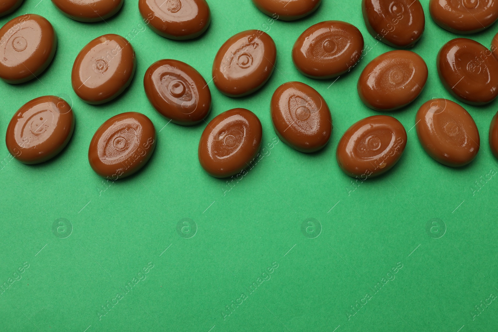 Many tasty caramel candies on green background, flat lay. Space for text Photo of Many tasty caramel candies on green background, flat lay. Space for text