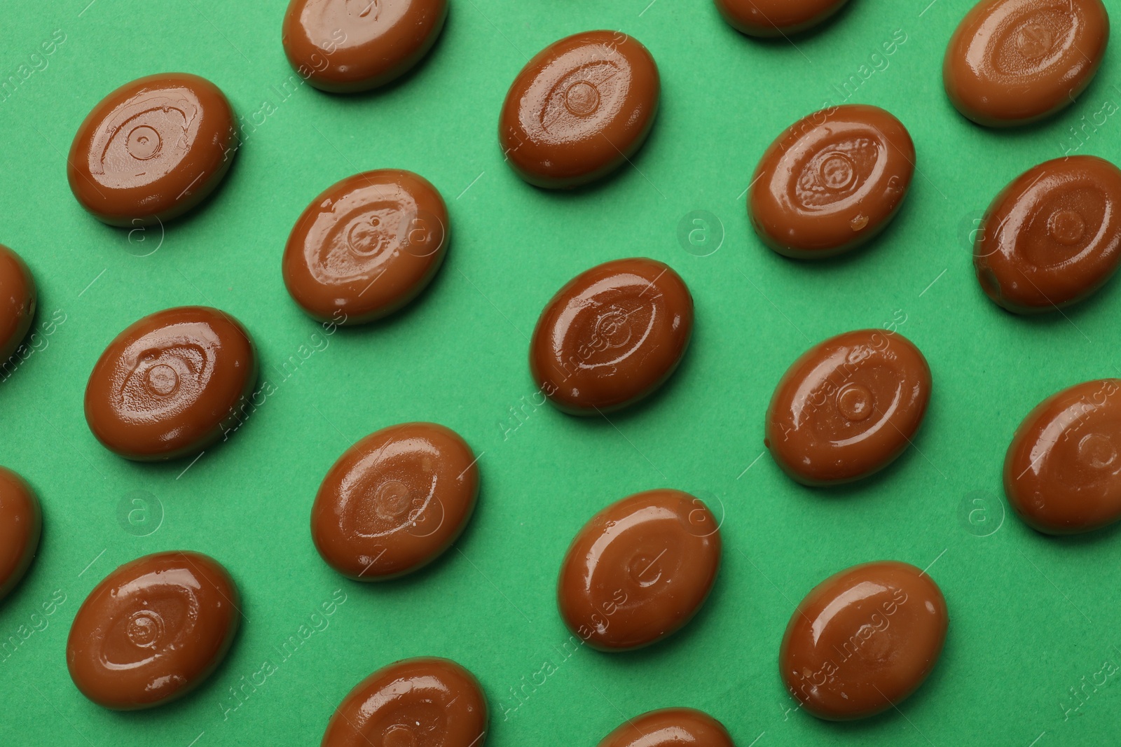 Many tasty caramel candies on green background, flat lay Photo of Many tasty caramel candies on green background, flat lay