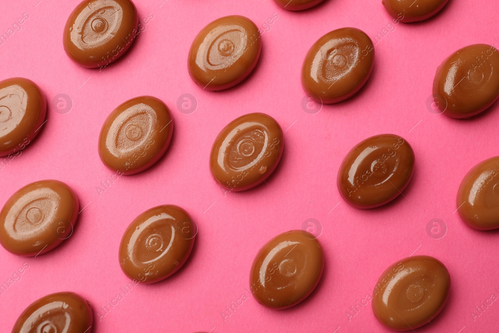 Many tasty caramel candies on pink background, flat lay Photo of Many tasty caramel candies on pink background, flat lay
